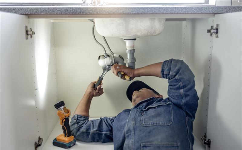 Plumber repairing pipes beneath a bathroom sink in Punta Gorda