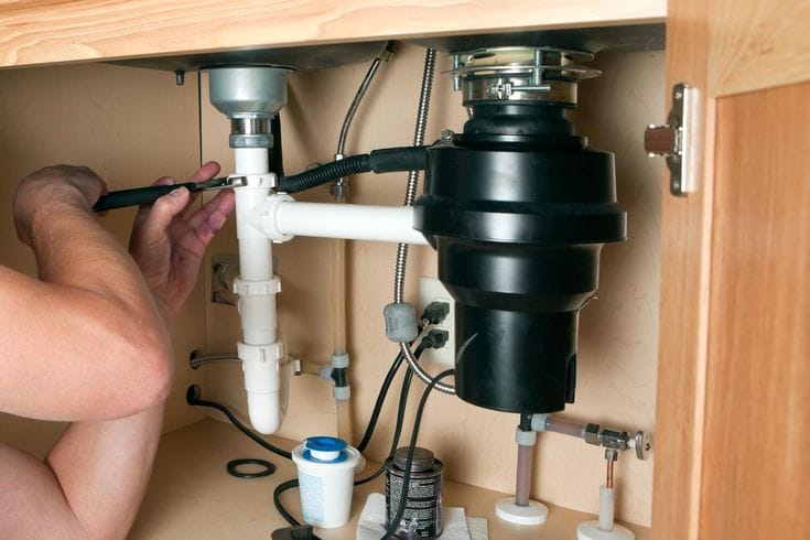 Plumber installing a garbage disposal beneath a kitchen sink in Punta Gorda