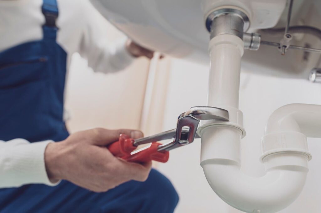 Plumber repairing a white drain pipe beneath a sink in Punta Gorda